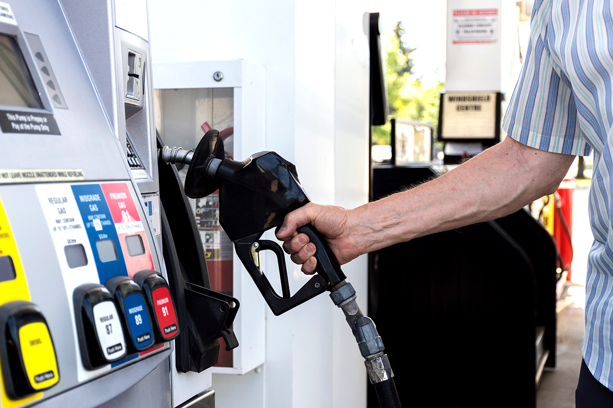 Photo of a person filling up a vehicle at a gas station holding a pump nozzle.