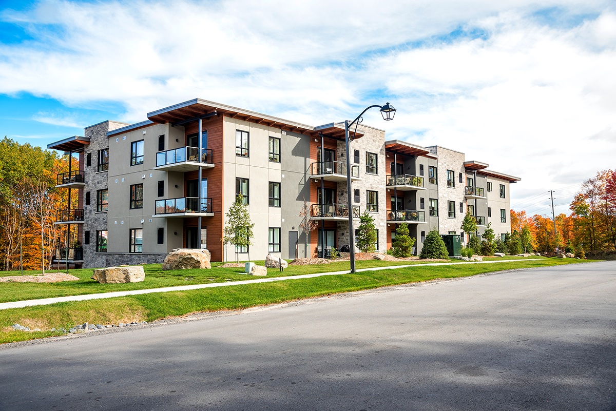 Photo of a brand new apartment building surrounded by colourful trees in a housing development on a partly cloudy autumn day. Huntsville, ON, Canada.