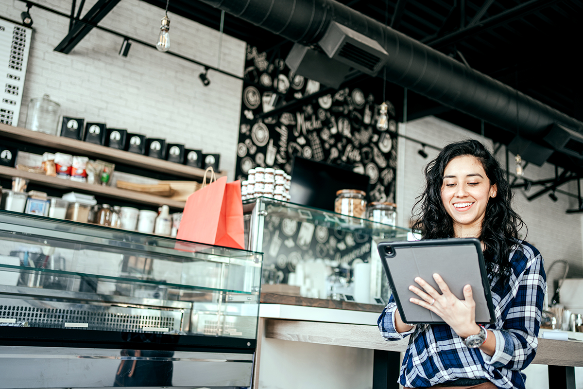 Photo of a shop owner smiling at the camera working on a tablet screen.