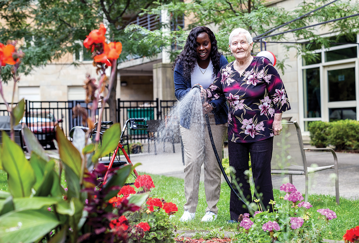 Photo of seniors and personal support workers enjoying the outdoor garden space at a long term care facility.