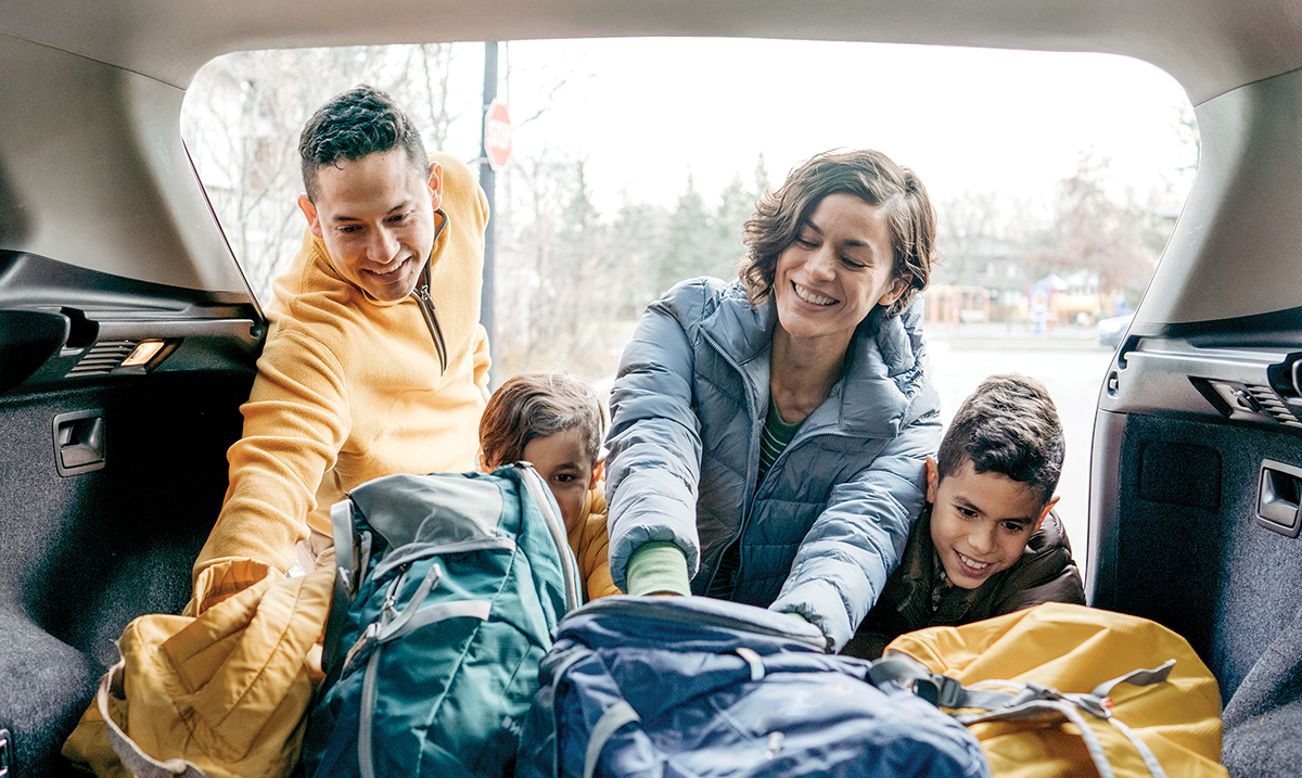 Photo of a family of four loading up a car with luggage. 